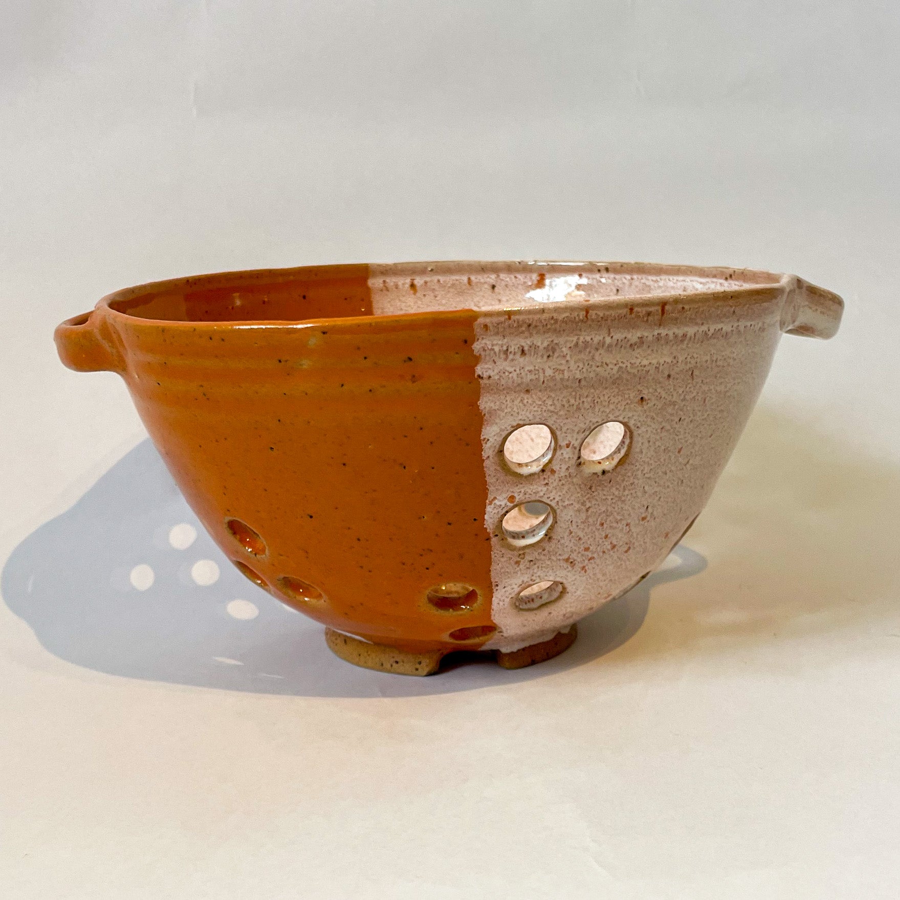 Small stoneware colander for washing small fruits and veg by Frankie Atkinson. Orange and cream dipped glaze.