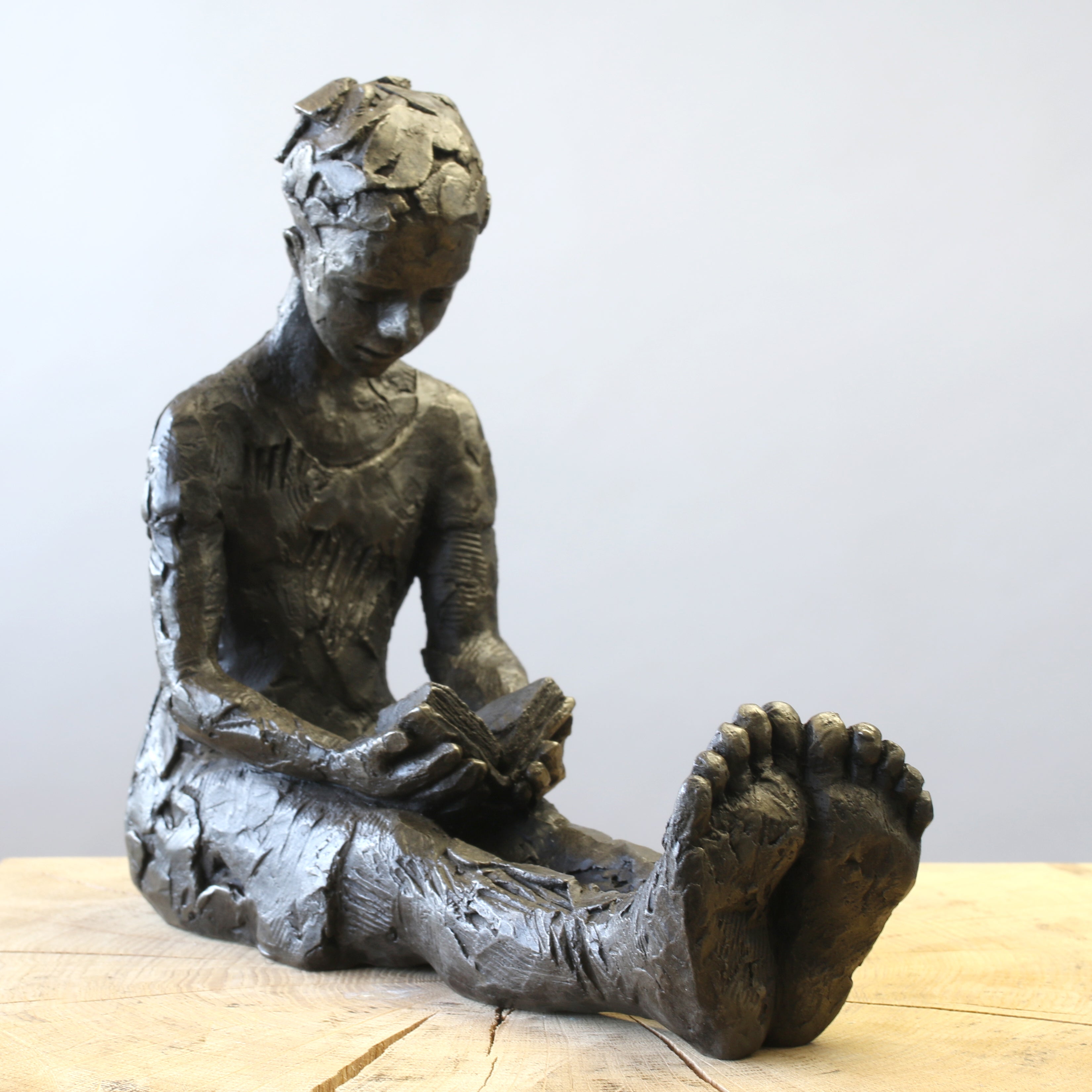 Bronze sculpture of girl reading a book by Carol Peace