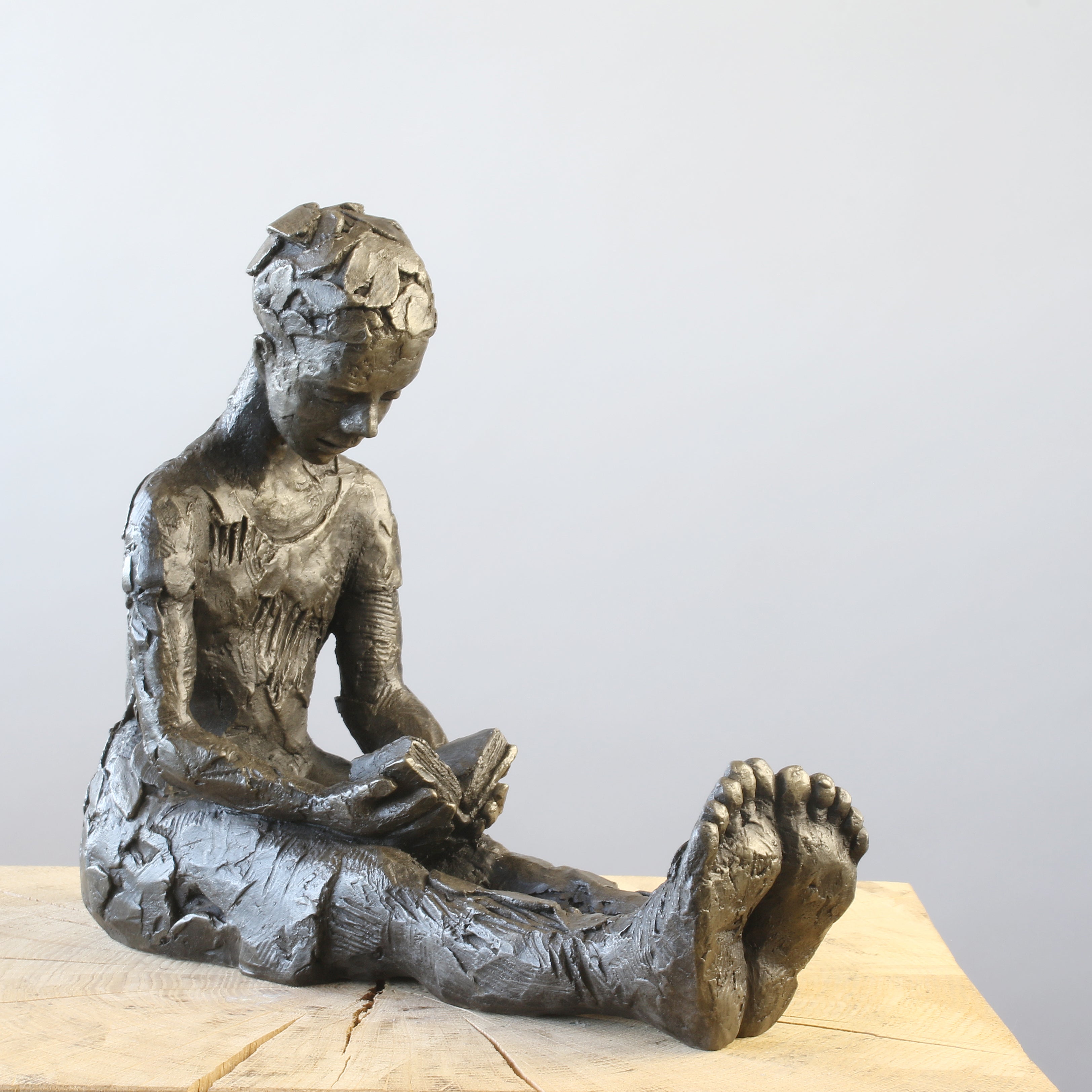 Bronze sculpture of girl reading a book by Carol Peace