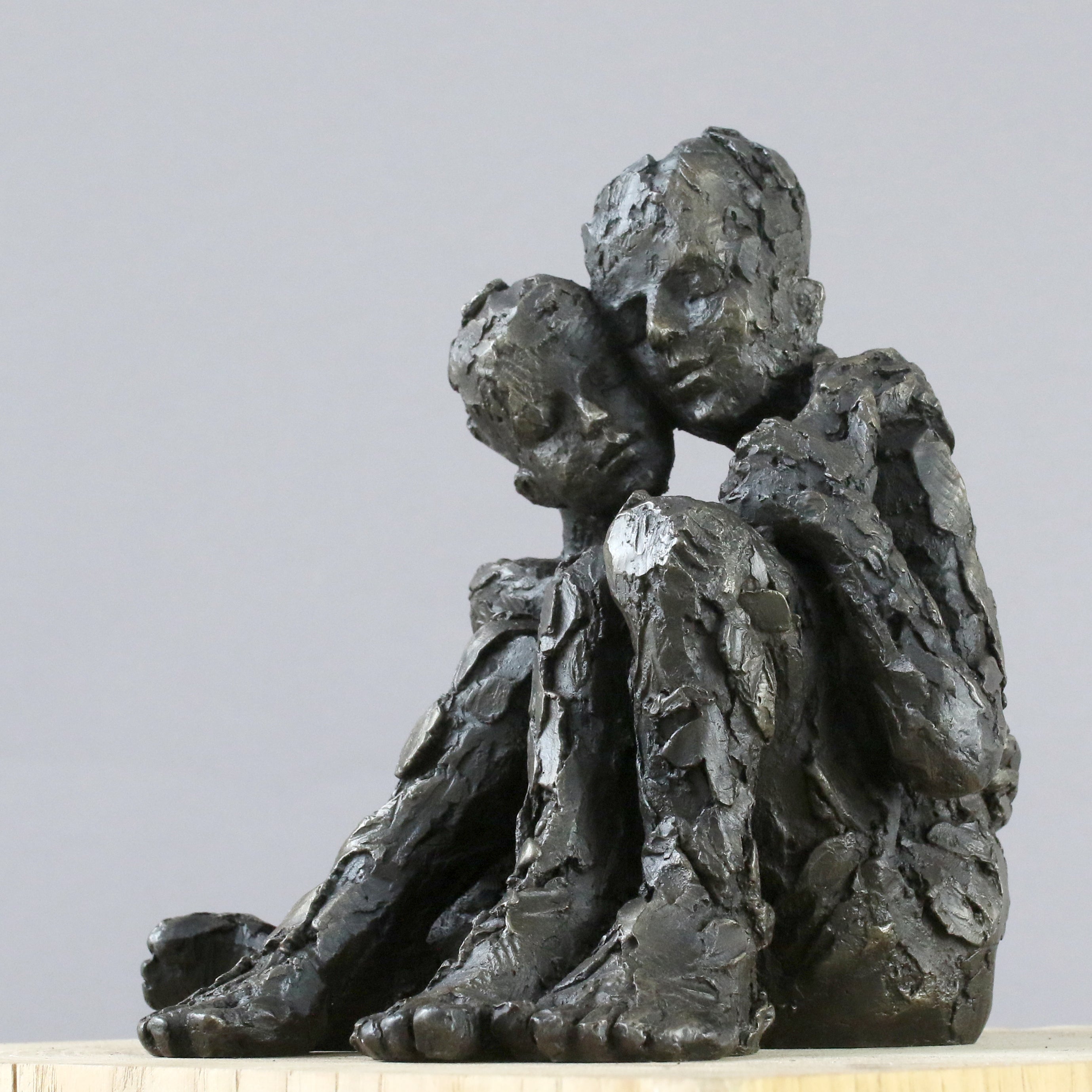 Iron resin sculpture of two huddled figures in embrace by Carol Peace