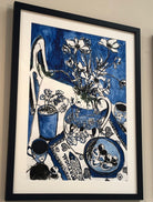 Painting in blue of table scape with decorative vase and flowers and Portugal towel