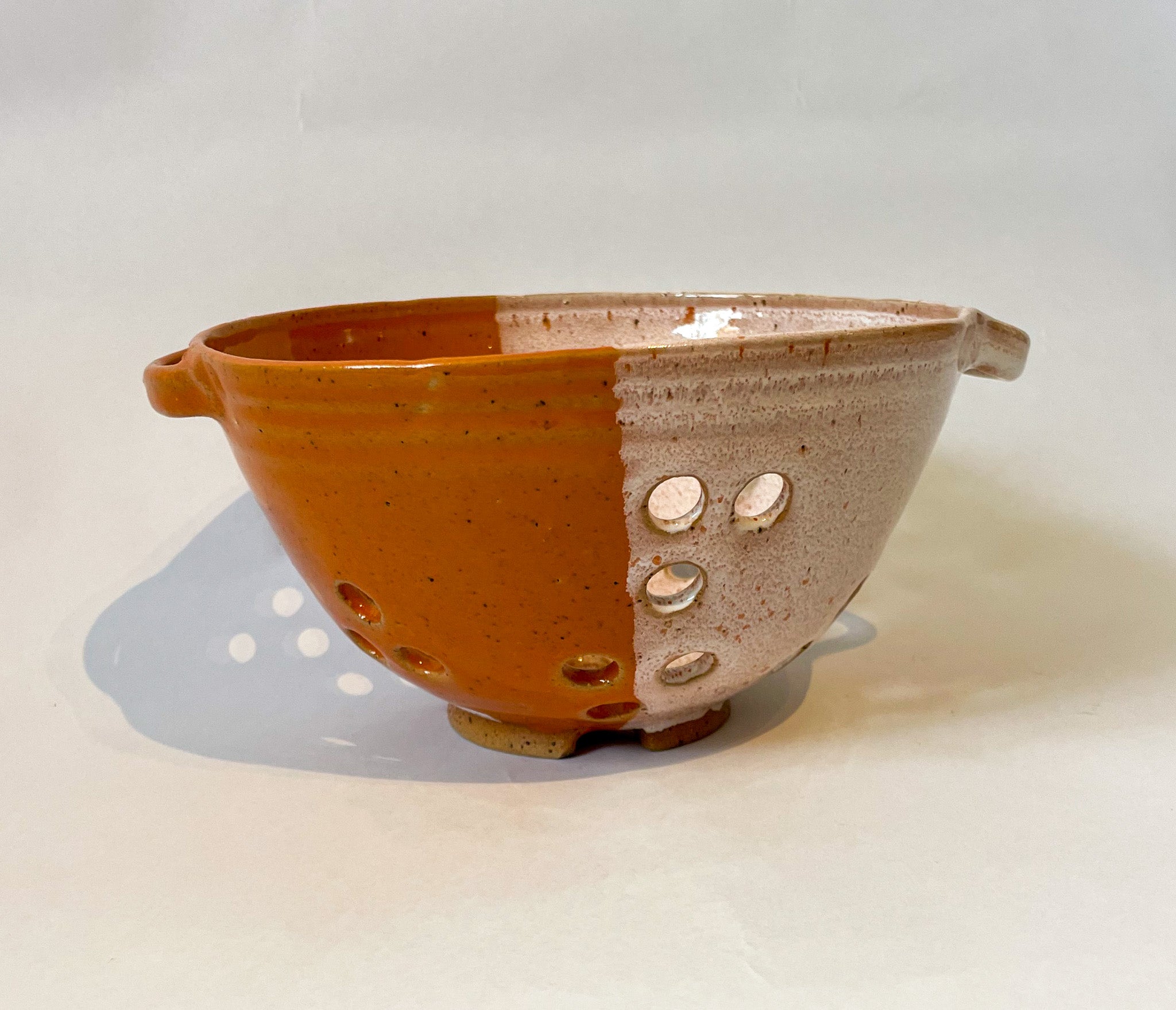 Small stoneware colander for washing small fruits and veg by Frankie Atkinson. Orange and cream dipped glaze.